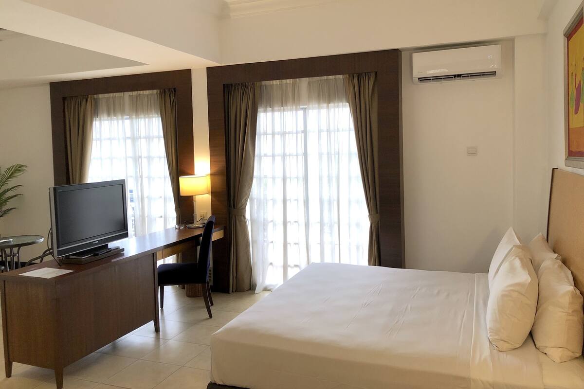 Une chambre d’hôtel avec un lit, un bureau avec une télévision, une chaise et des rideaux.