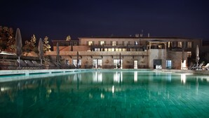 Vista nocturna de un hotel con piscina, sillas de descanso y un edificio con múltiples ventanas y balcones.