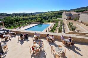 Un espacio para comer al aire libre con piscina y vistas a un paisaje montañoso.
