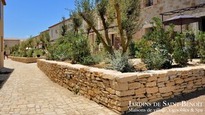 Un sendero de piedra que lleva a una hilera de edificios tradicionales de piedra con mesas al aire libre y sombrillas.