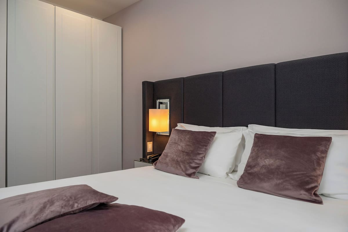 A neatly made bed with white and brown pillows, a bedside lamp, and a wardrobe with sliding doors.
