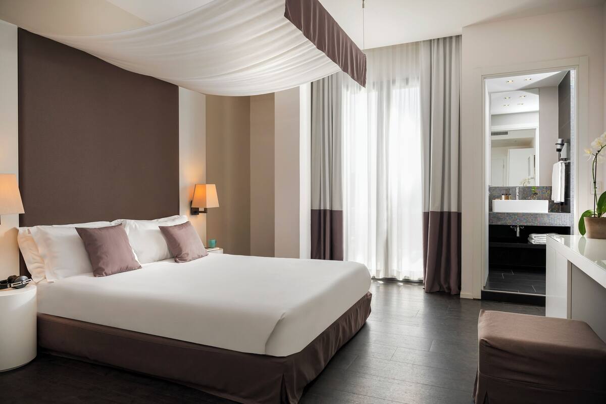 A hotel room with a large bed, bedside lamps, a desk with a mirror, and a view of the bathroom.