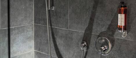 Una ducha moderna con cabezal de ducha de mano y ducha de lluvia, montada en una pared con azulejos oscuros.