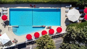 A large rectangular swimming pool with a tiled deck surrounding it, equipped with sun loungers and umbrellas.