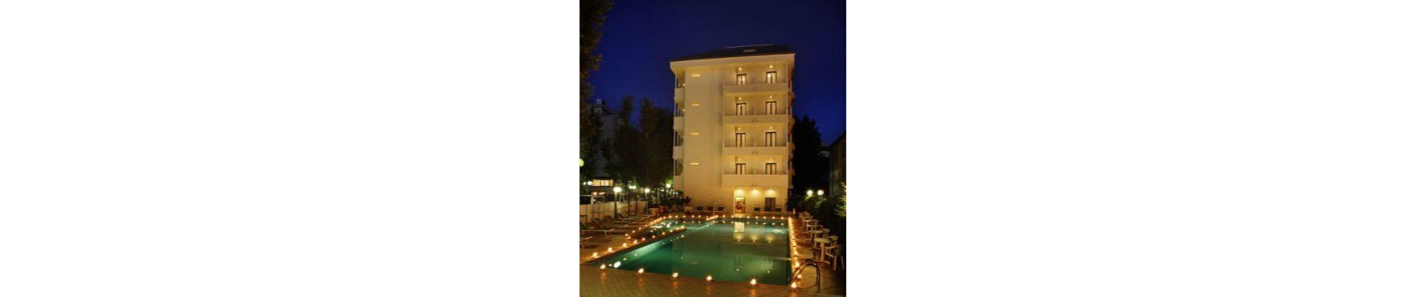 Un hotel de varios pisos con piscina al frente, rodeado de árboles y mobiliario exterior.