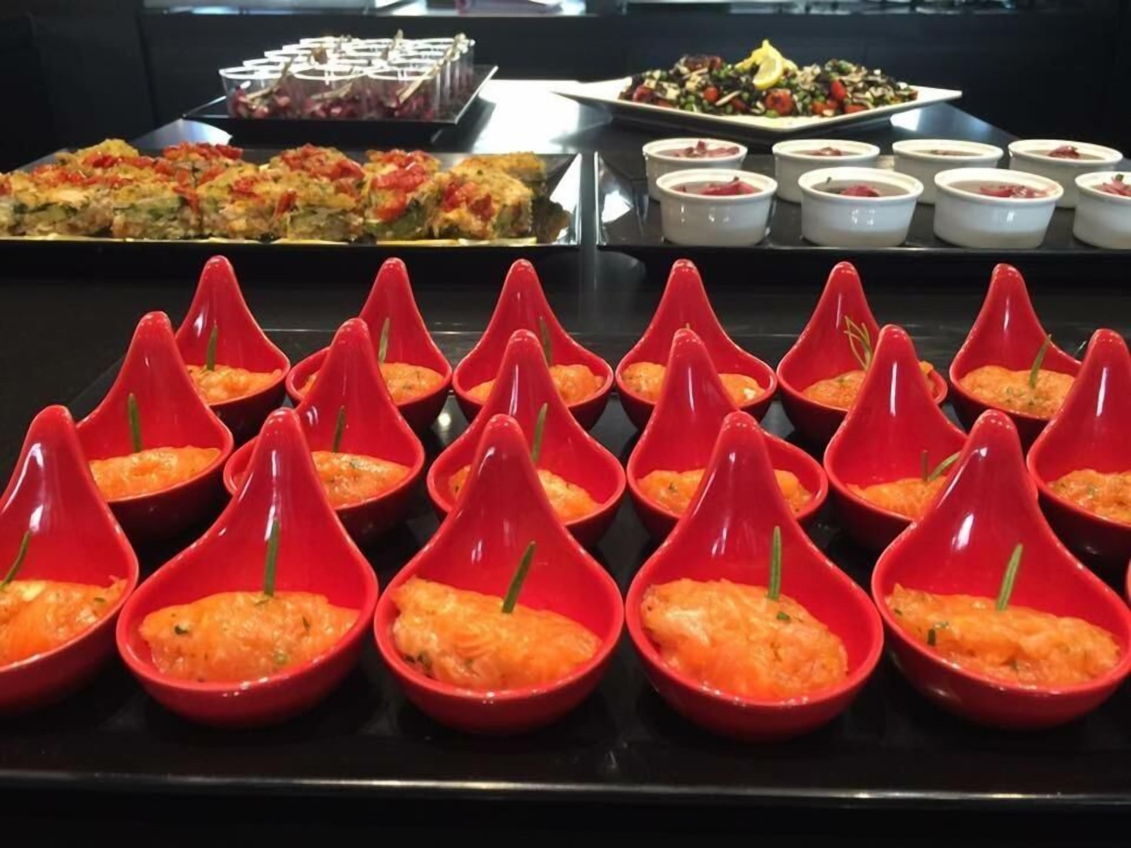 A buffet with various dishes including a red dish with a green garnish, a tray of food with red and green toppings, and several small white bowls with food.