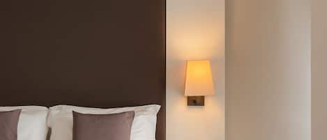 A neatly made bed with white and brown bedding, a bedside lamp, and a small side table with a book and a teal mug.