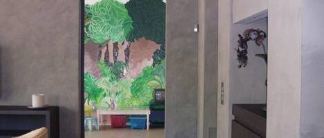 Un pasillo que conduce a una habitación con un mural de árboles y un televisor sobre un soporte.