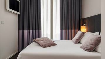 Ein Hotelzimmer mit einem Bett, zwei Kissen, einem Nachttisch mit Lampe und einem Fenster mit Vorhängen.