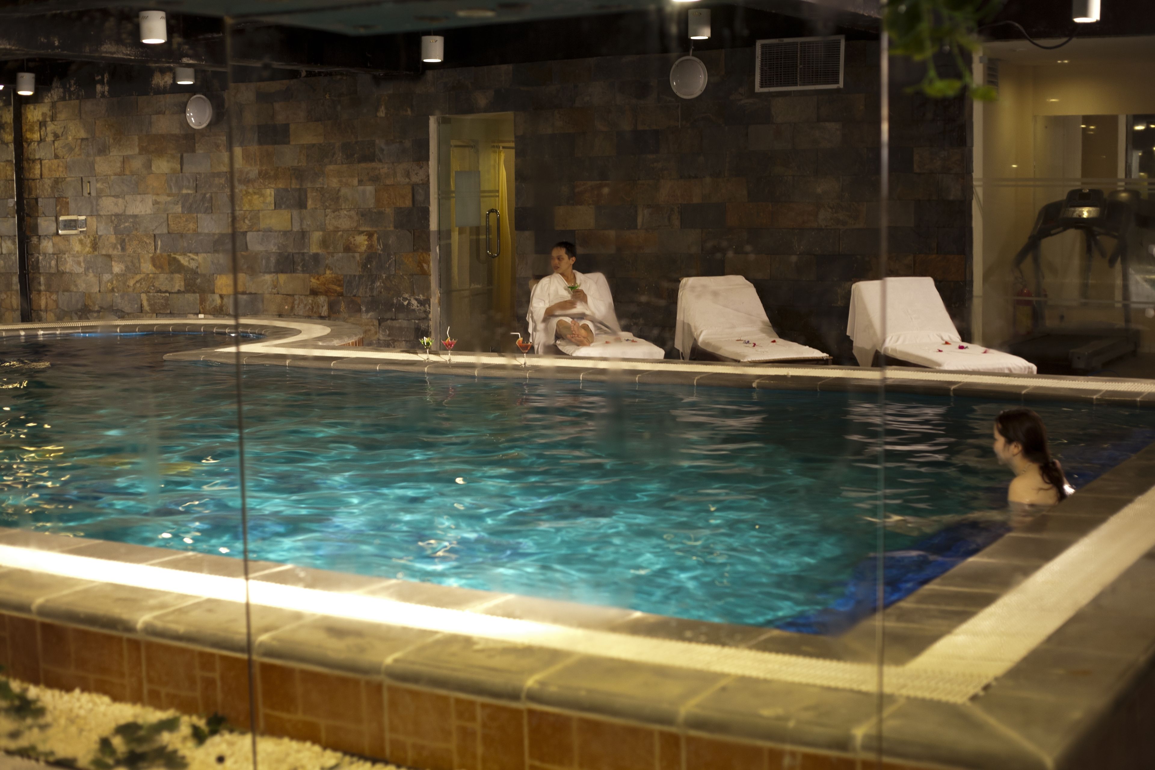 An indoor swimming pool with a stone wall, a door, and two lounge chairs.