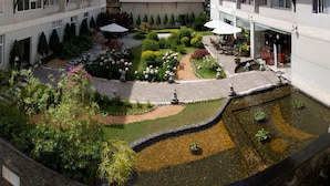 A courtyard with a central water feature, surrounded by neatly arranged plants and a seating area with umbrellas. - Muong Thanh Da Lat (Xuan Huong - Da Lat)