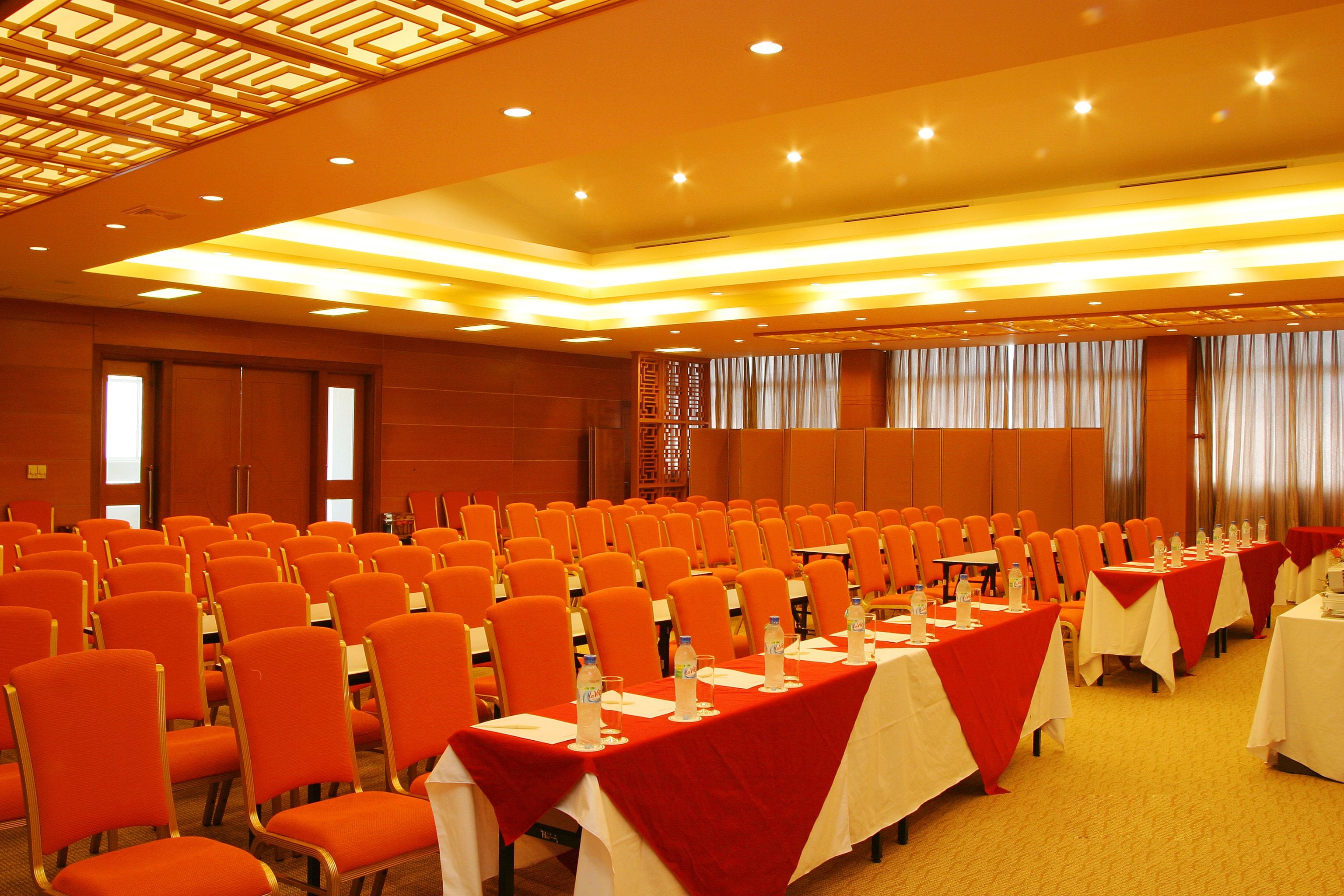 A conference room with rows of orange chairs and tables set up for a meeting.