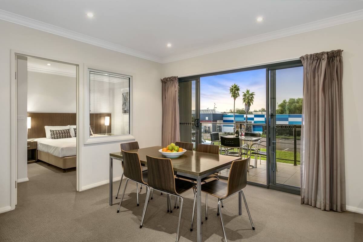 Habitación de hotel moderna con comedor, cama y balcón con vistas a la ciudad.