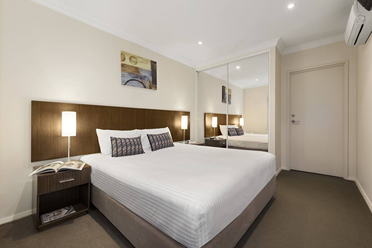Una habitación de hotel con una cama grande, mesitas de noche, un espejo y una puerta.