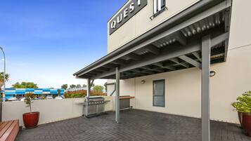 An outdoor patio area with a barbecue grill, potted plants, and a sign that reads "QUEST."