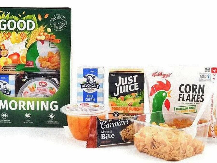 Uma mesa de café da manhã com Good Morning, iogurte integral Devondale, suco Paradise da Just Juice, Corn Flakes Kellogg's e Muesli Bite da Carman's.