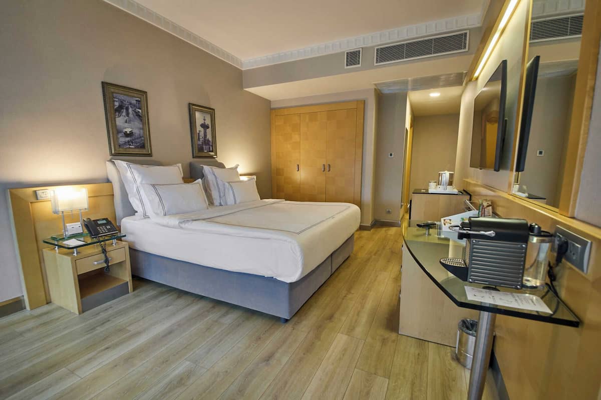 Une chambre d’hôtel comprenant un lit, une table de chevet, une lampe, une armoire et un bureau avec un miroir.