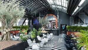 Un espacio interior moderno con suelo a rayas blanco y negro, zonas de estar y un árbol grande.
