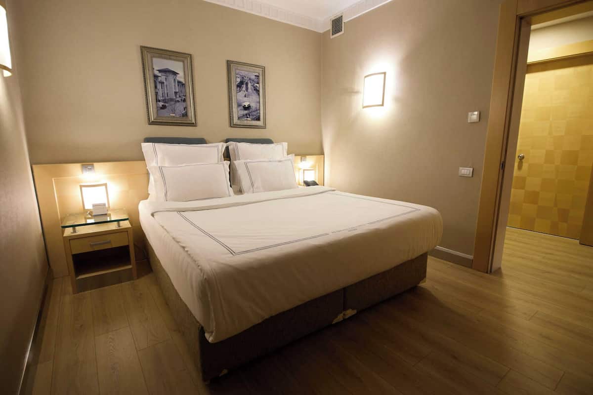 Une chambre d’hôtel avec un grand lit, deux tables de chevet avec des lampes et deux tableaux encadrés au mur.