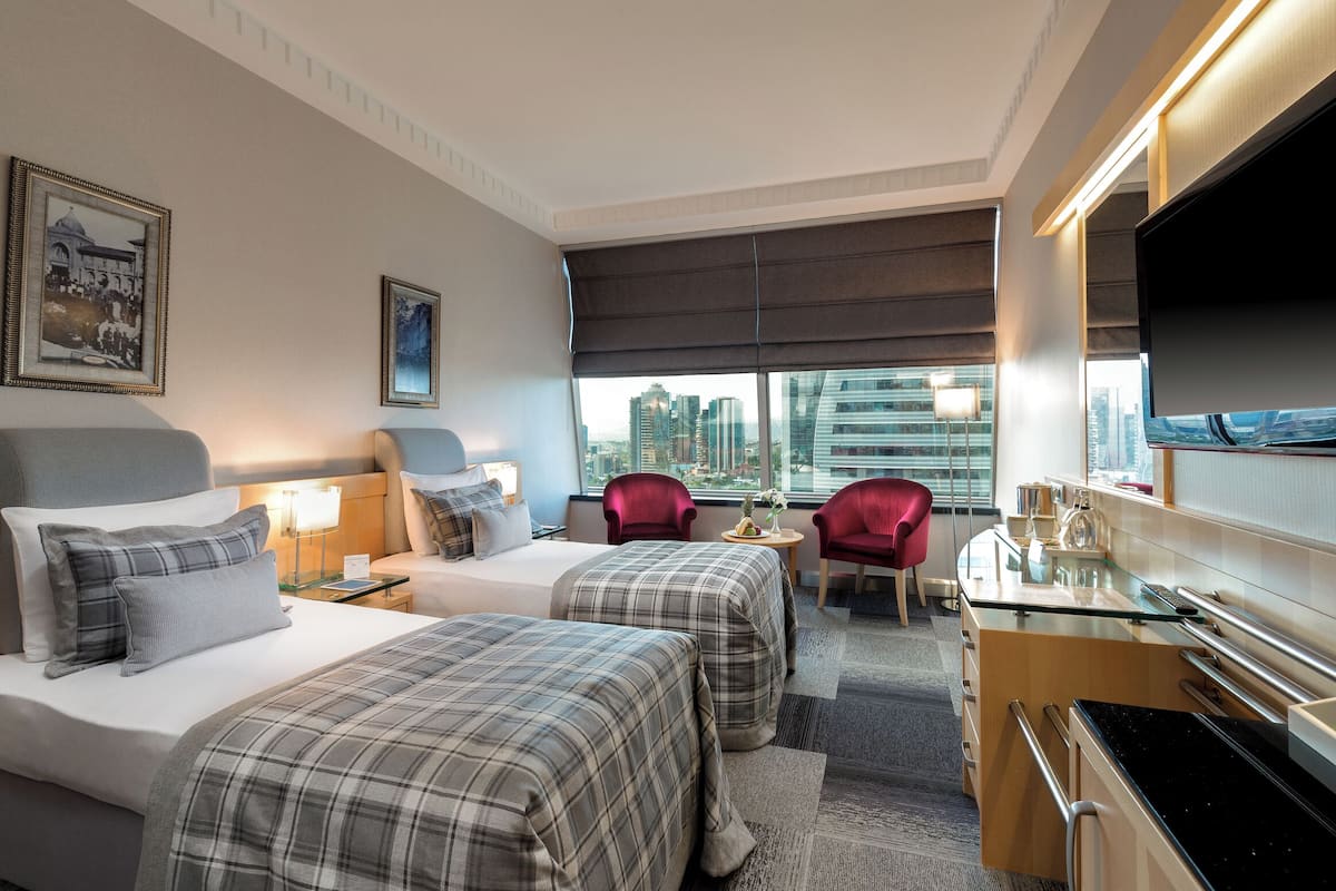 Une chambre d’hôtel avec deux lits, un bureau, une télévision et une vue sur la ville.