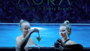 Dos personas en una piscina con un letrero que dice "AURA Serenity in Every Breath".