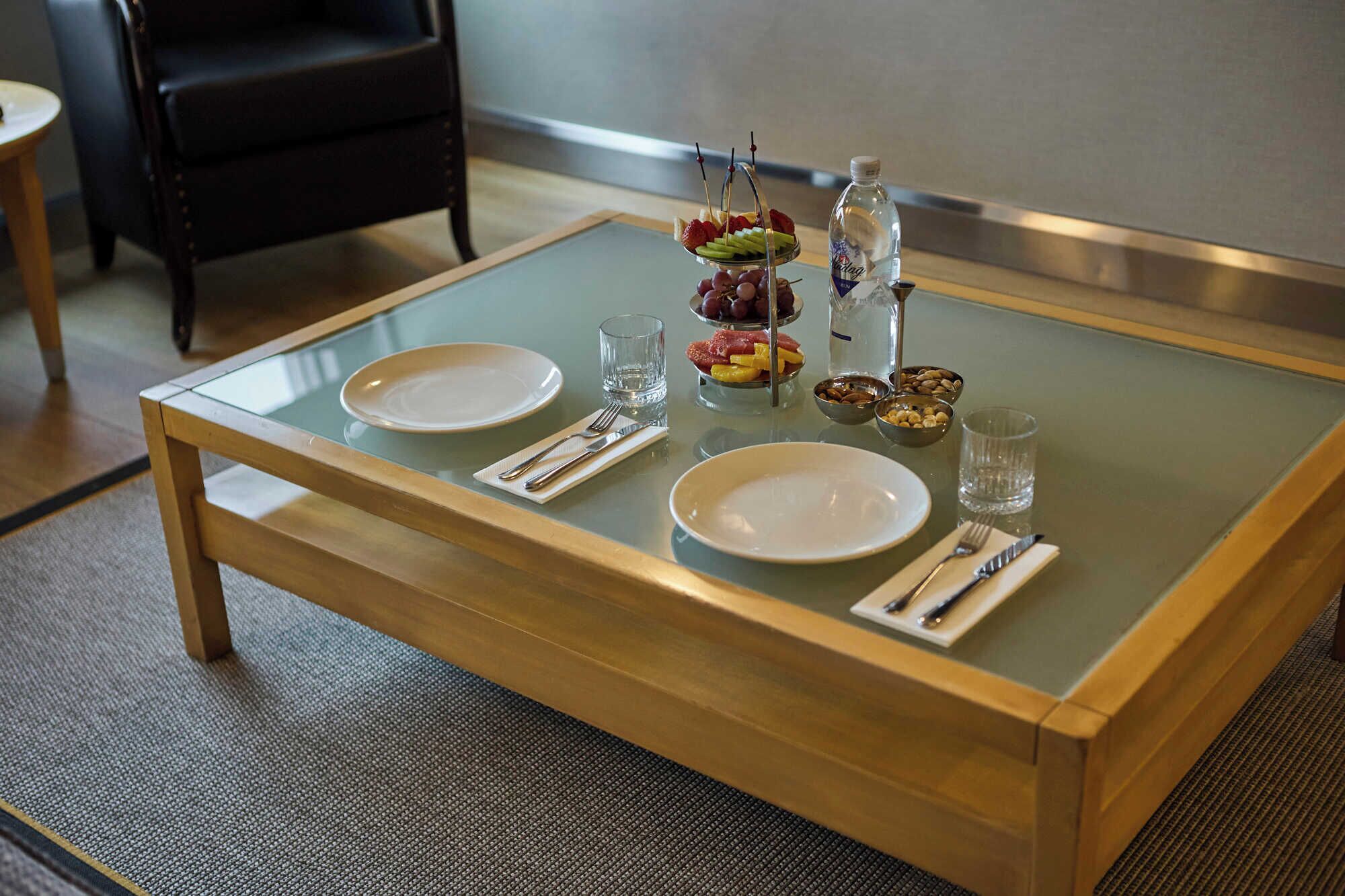 A dining table with two plates, cutlery, glasses, and a fruit basket.