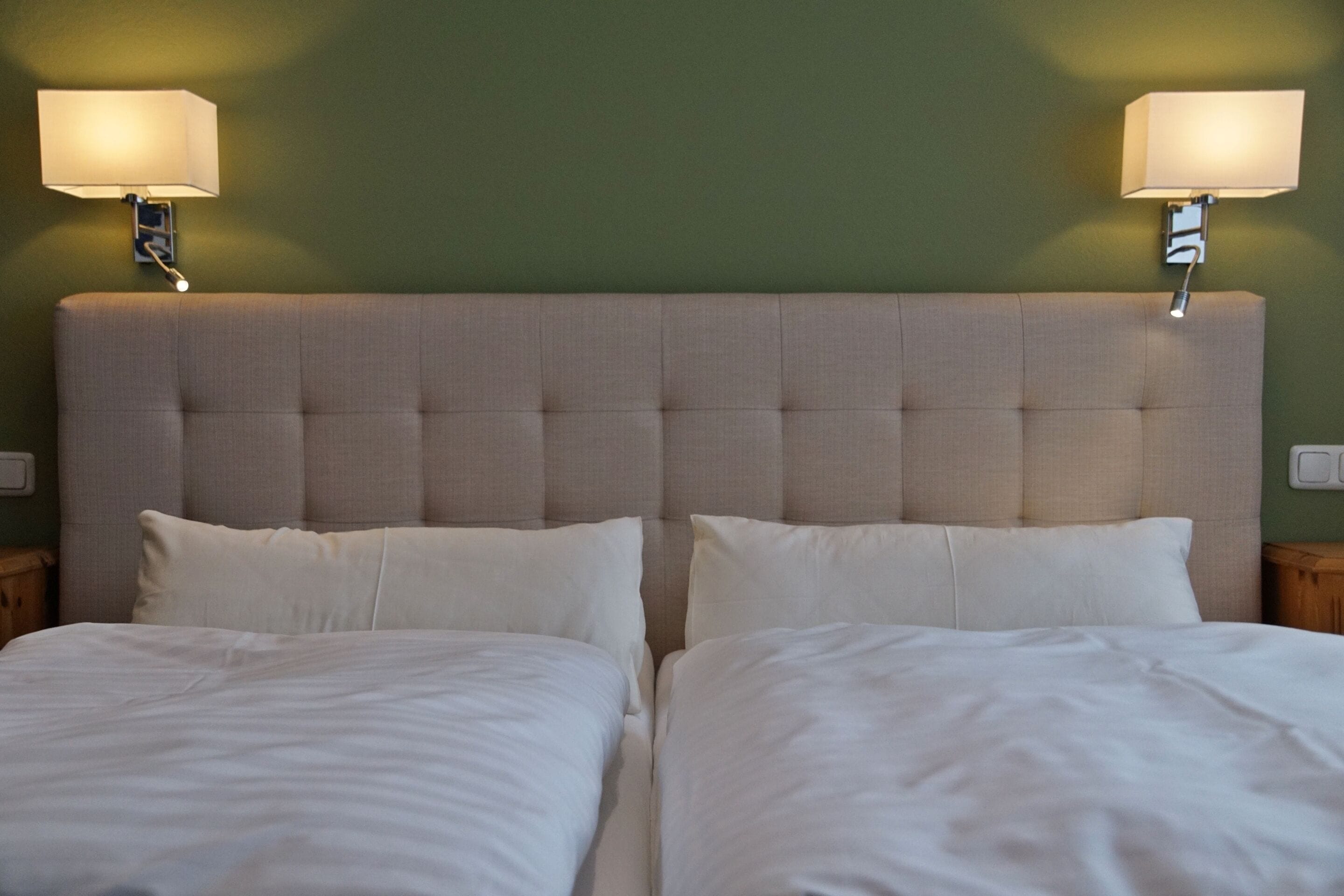 Uma cama de casal com cabeceira estofada, duas luminárias de apoio e uma parede verde.
