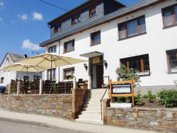 A two-story building with a stone facade, a wooden staircase leading to the entrance, and a signboard indicating a restaurant.