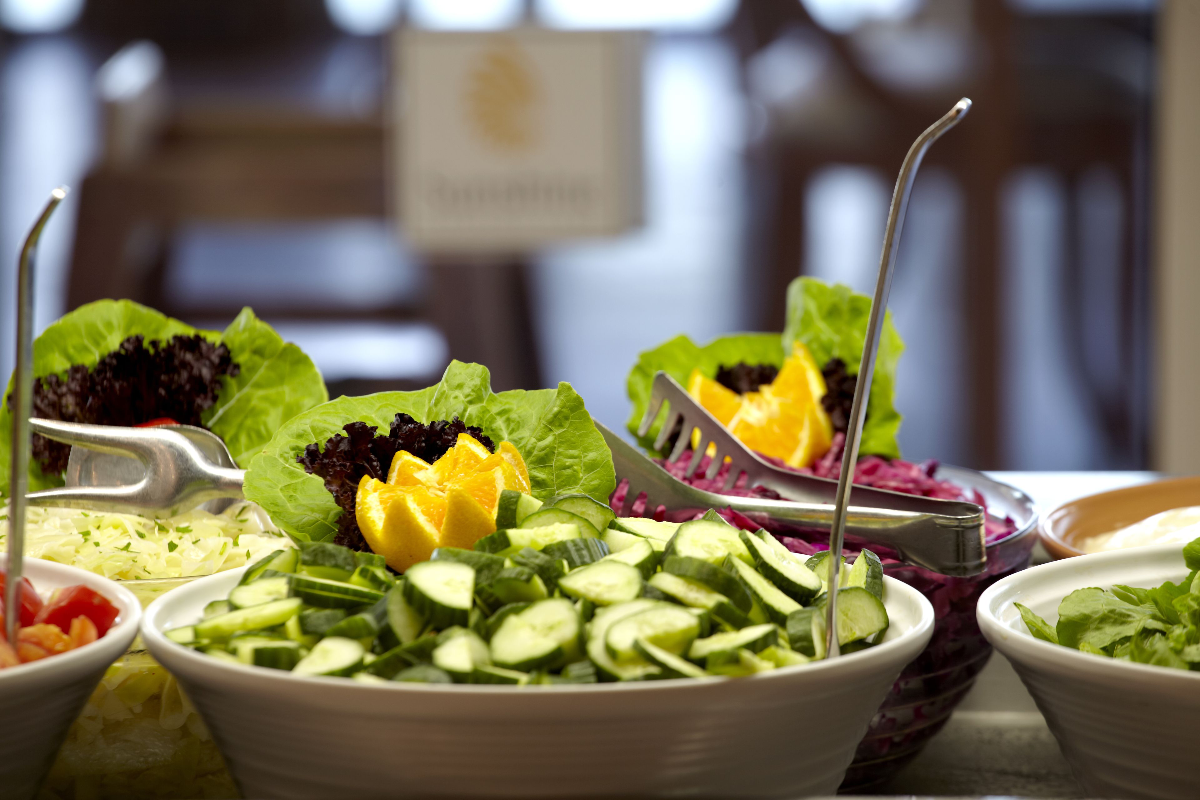 Verschiedene Salate mit unterschiedlichem Gemüse und Obst, auf einem Tisch mit Salatbesteck angerichtet.