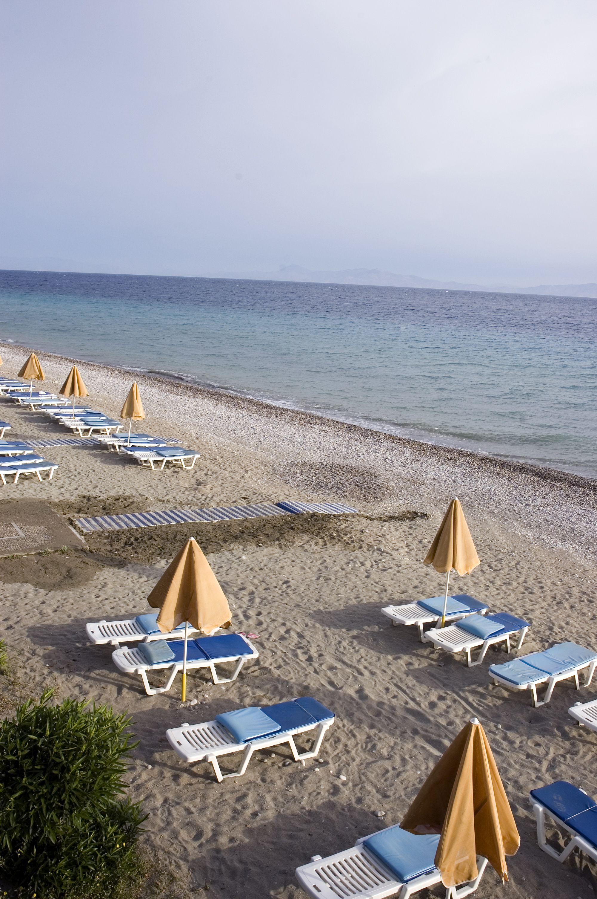 Una spiaggia con file di lettini e ombrelloni, vista libera sul mare e una battigia sabbiosa.