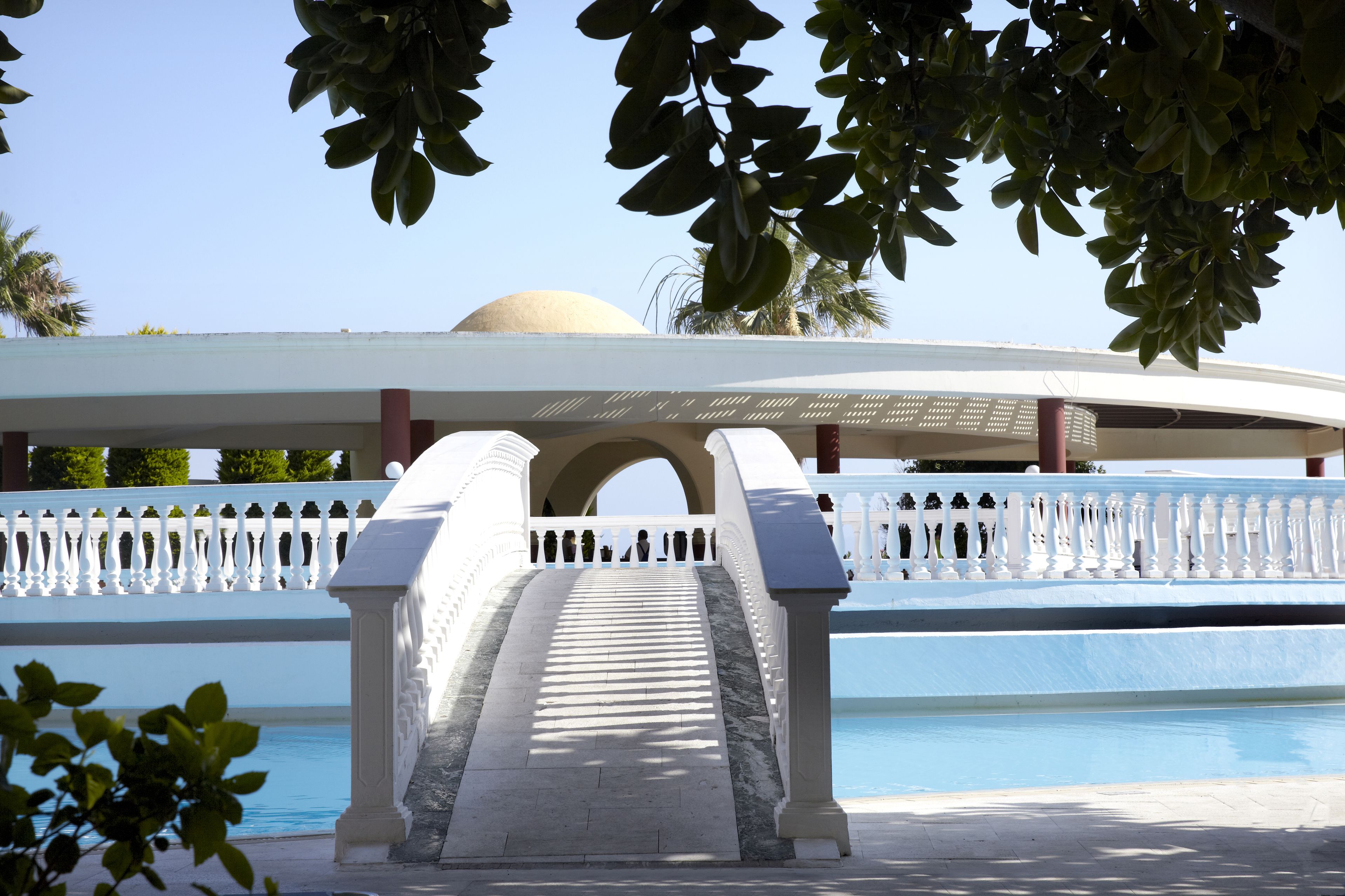 Zona de piscina con balaustrada blanca y una estructura abovedada al fondo.