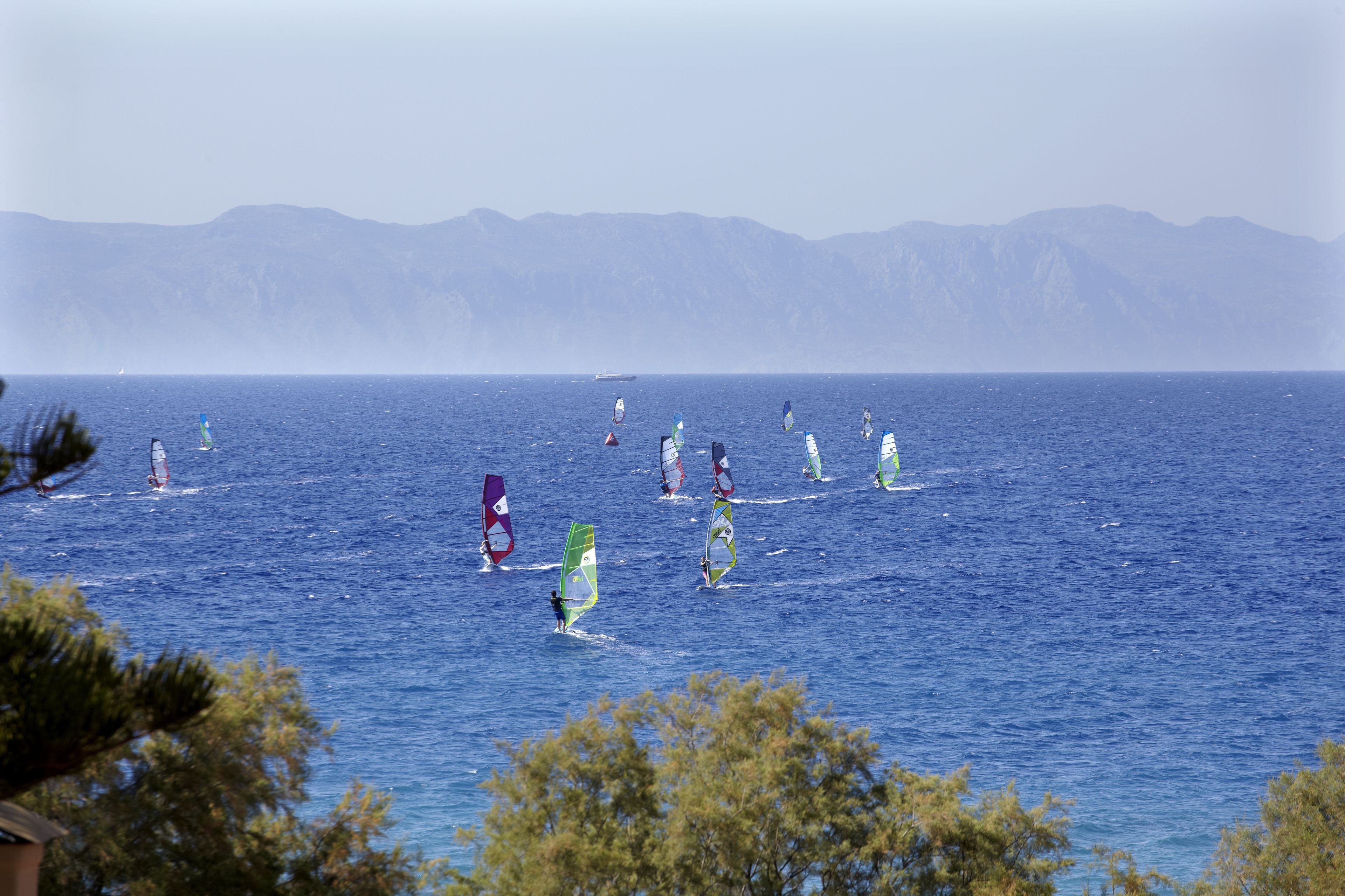 A coastal view with windsurfers on the water and mountains in the background.