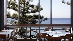 A dining area with a view of the sea and pine trees.