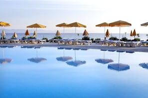 A poolside area with lounge chairs and umbrellas, a clear view of the sea, and a calm pool reflecting the surroundings.