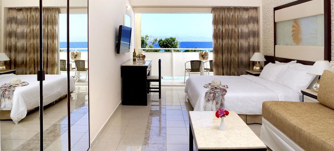 A hotel room with a bed, a desk, a chair, a small table with a vase, and a TV.