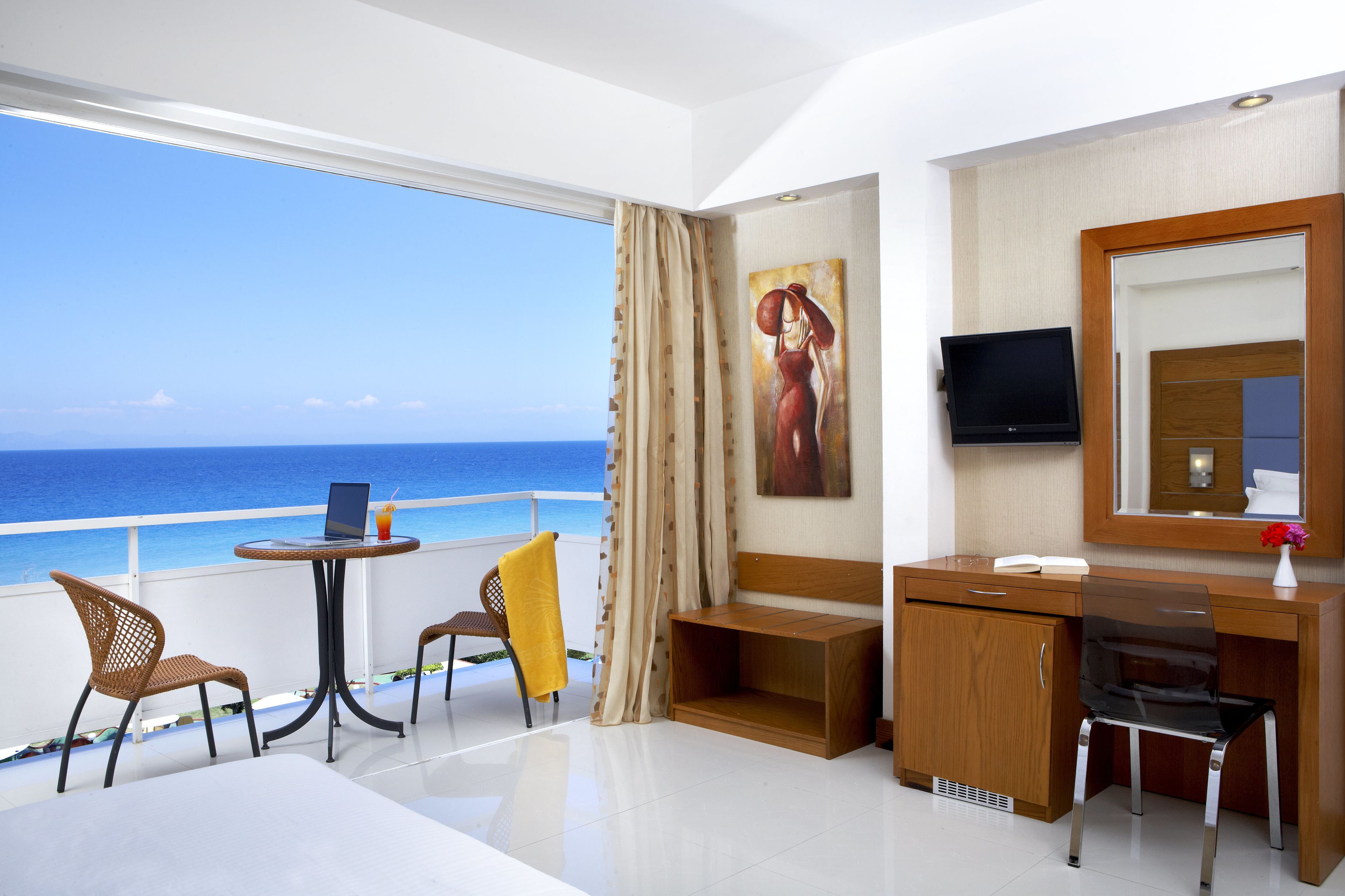 A hotel room with a balcony, a desk, a chair, a TV, and a painting.