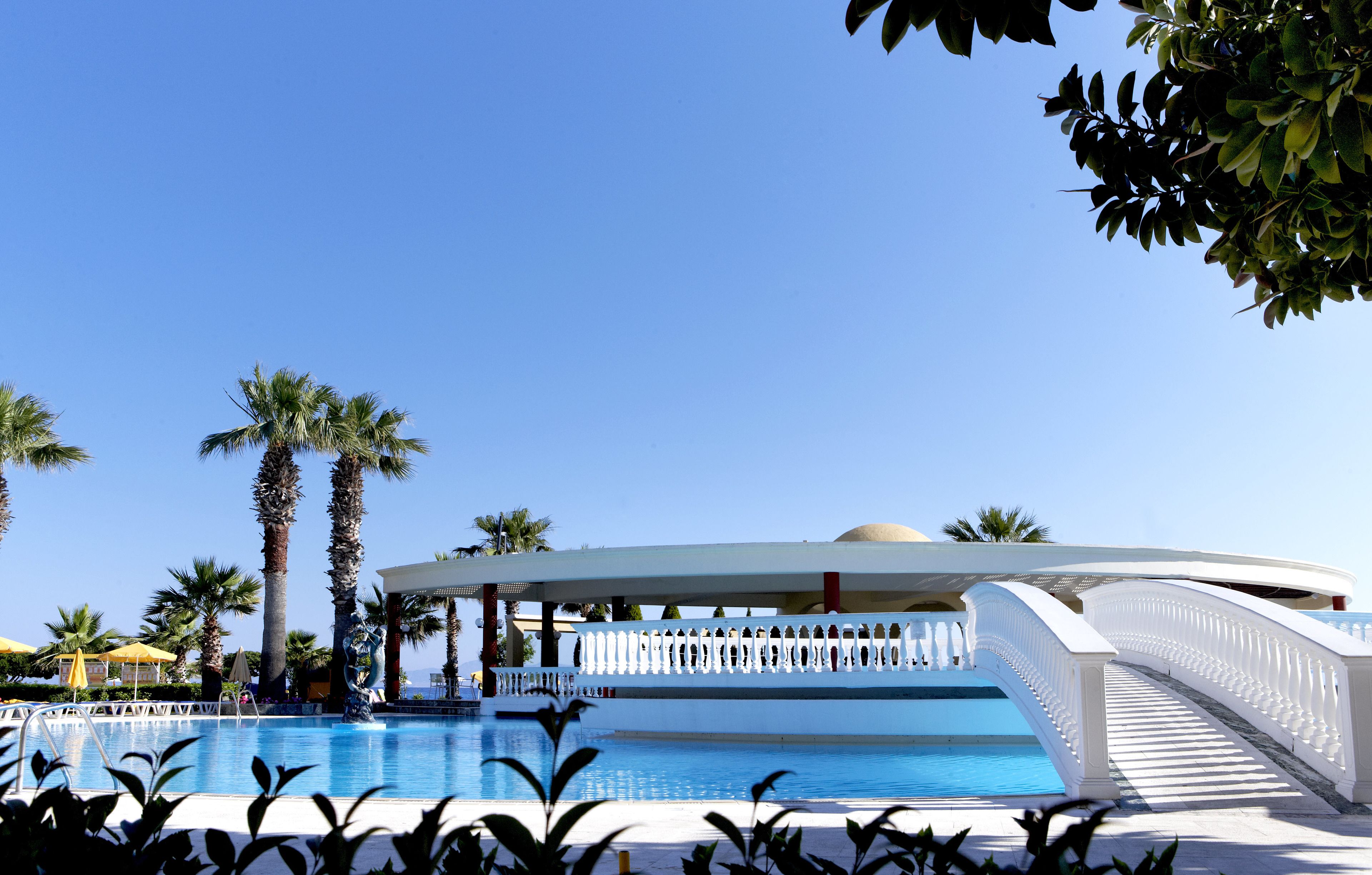 A pool area with a white bridge, palm trees, and a covered seating area.
