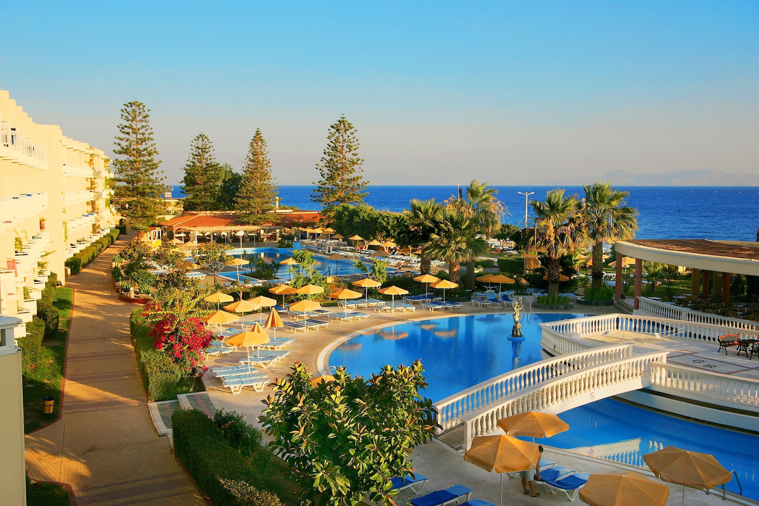 A resort with a large pool, sun loungers, umbrellas, and a view of the sea.