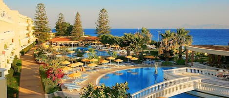 A resort with a large pool, sun loungers, umbrellas, and a view of the sea.