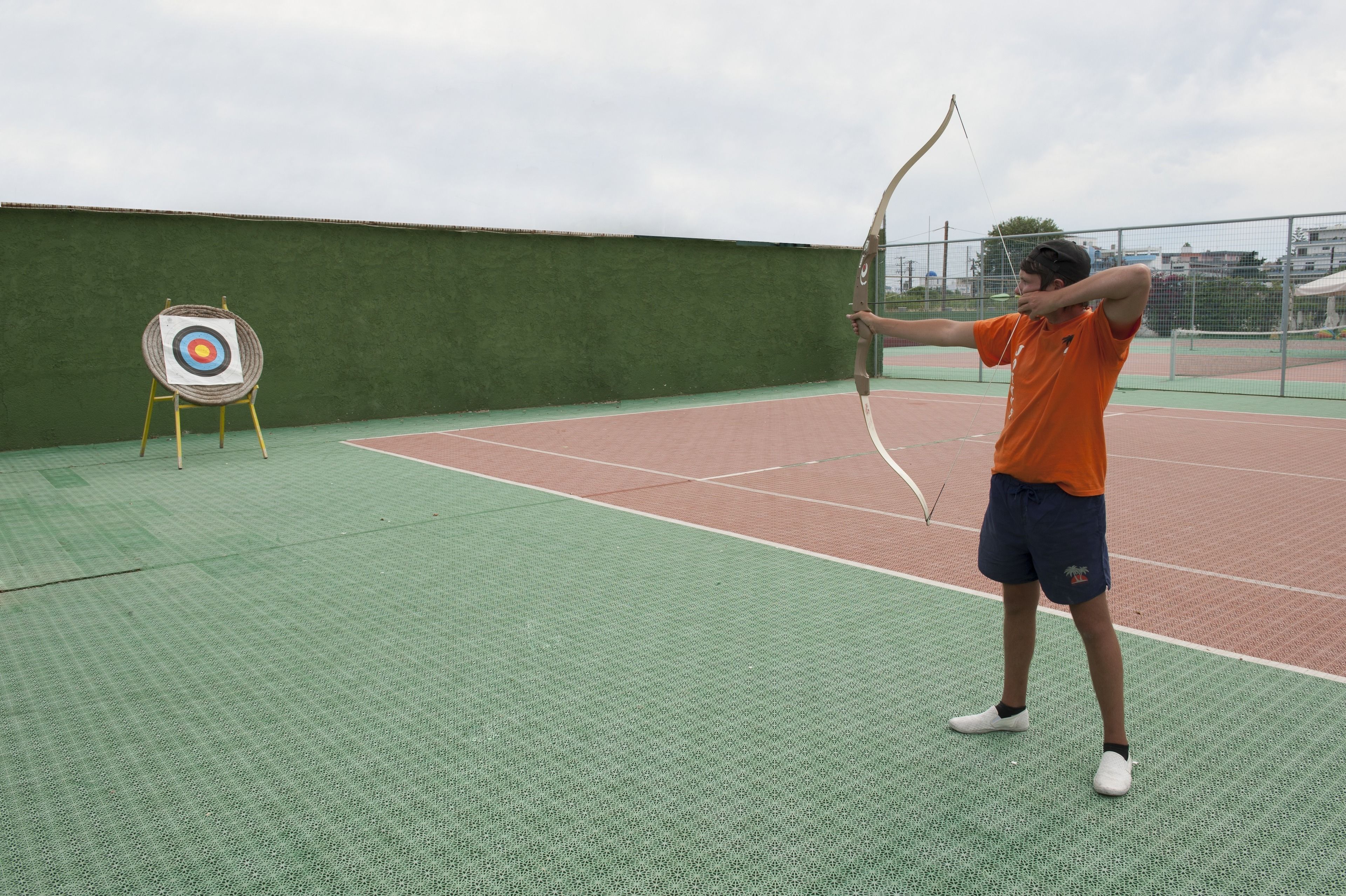 Una persona practicando tiro con arco en una cancha verde al aire libre, con un blanco de tiro al fondo.