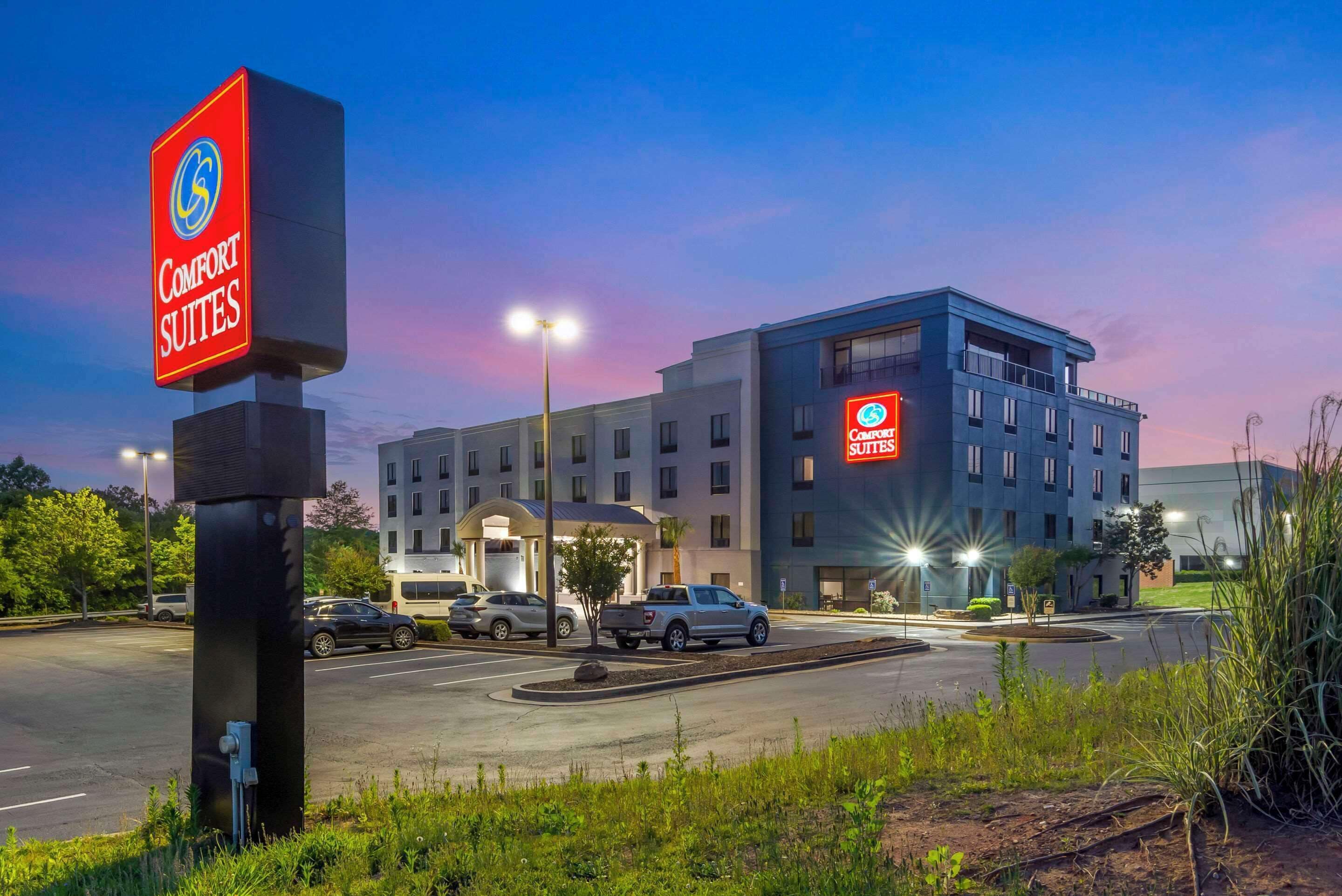 Un hotel Comfort Suites con diseño moderno, un estacionamiento y cielo despejado al atardecer.