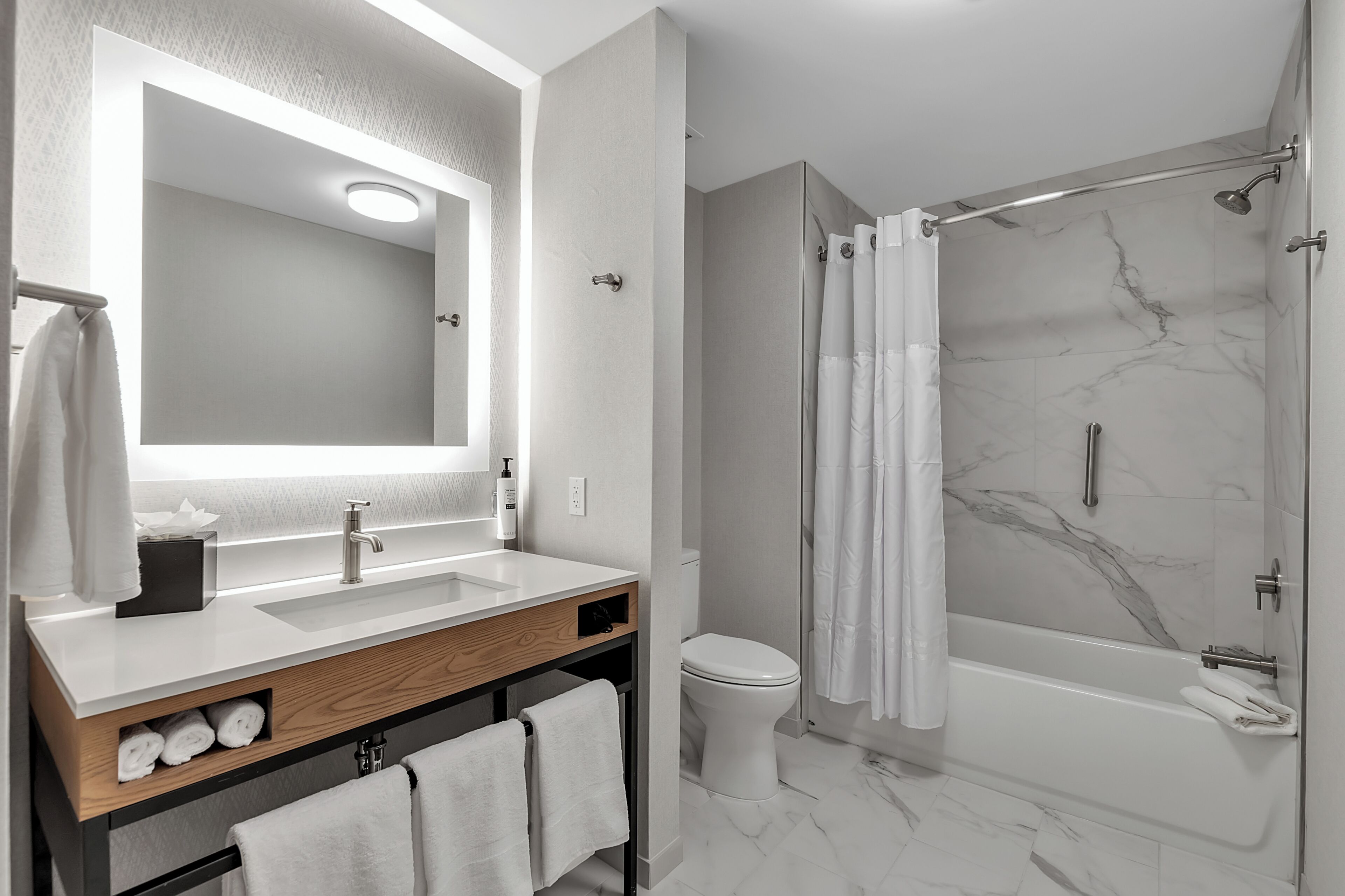 A modern bathroom with a large mirror, two sinks, a toilet, and a walk-in shower.