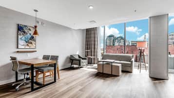 A modern living room with a dining area, large windows, and a city view.