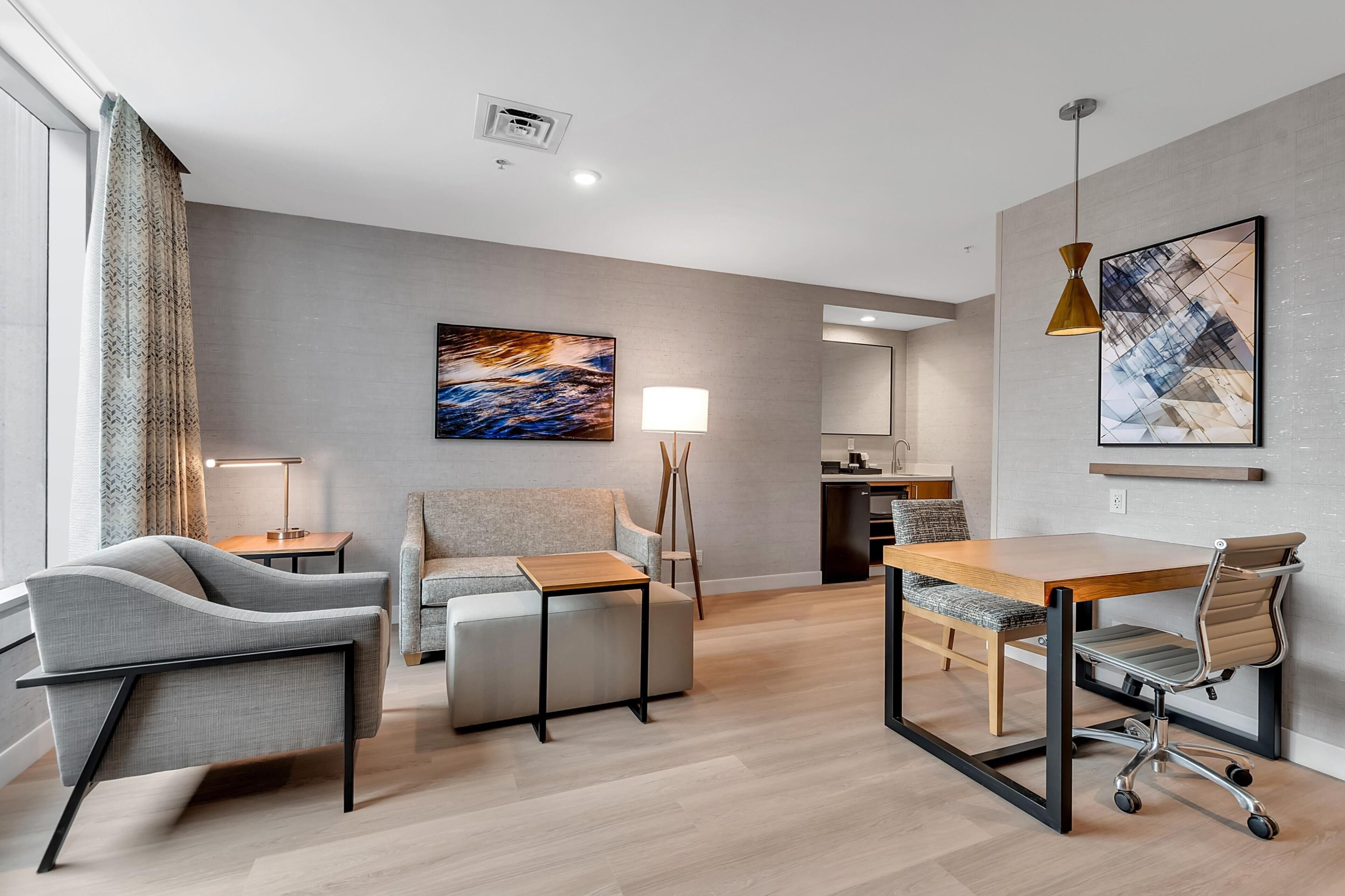 A modern hotel room with a sofa, a desk, a chair, a lamp, and artwork on the walls.