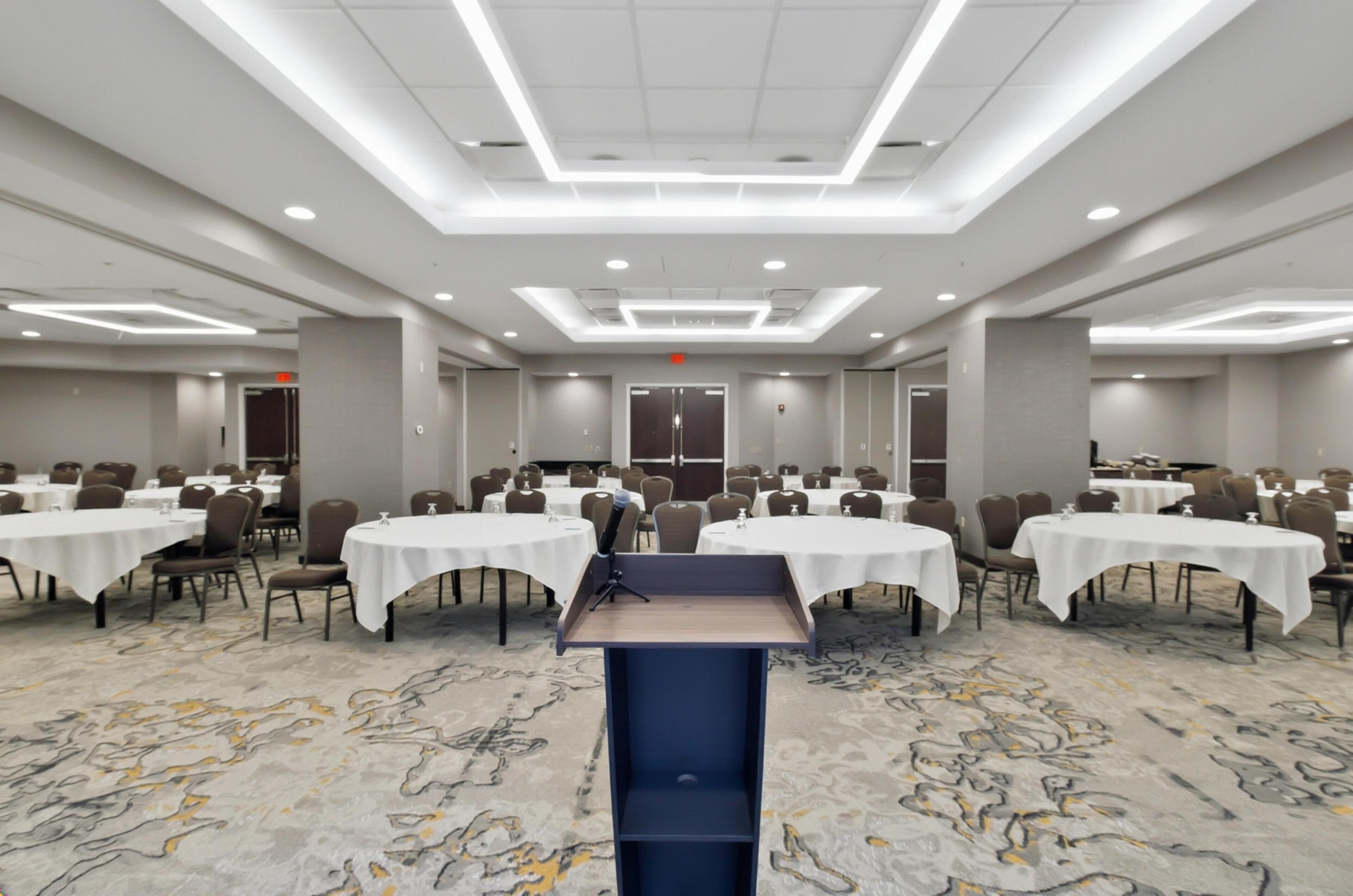 A large conference room with multiple tables, a podium, and a carpeted floor.
