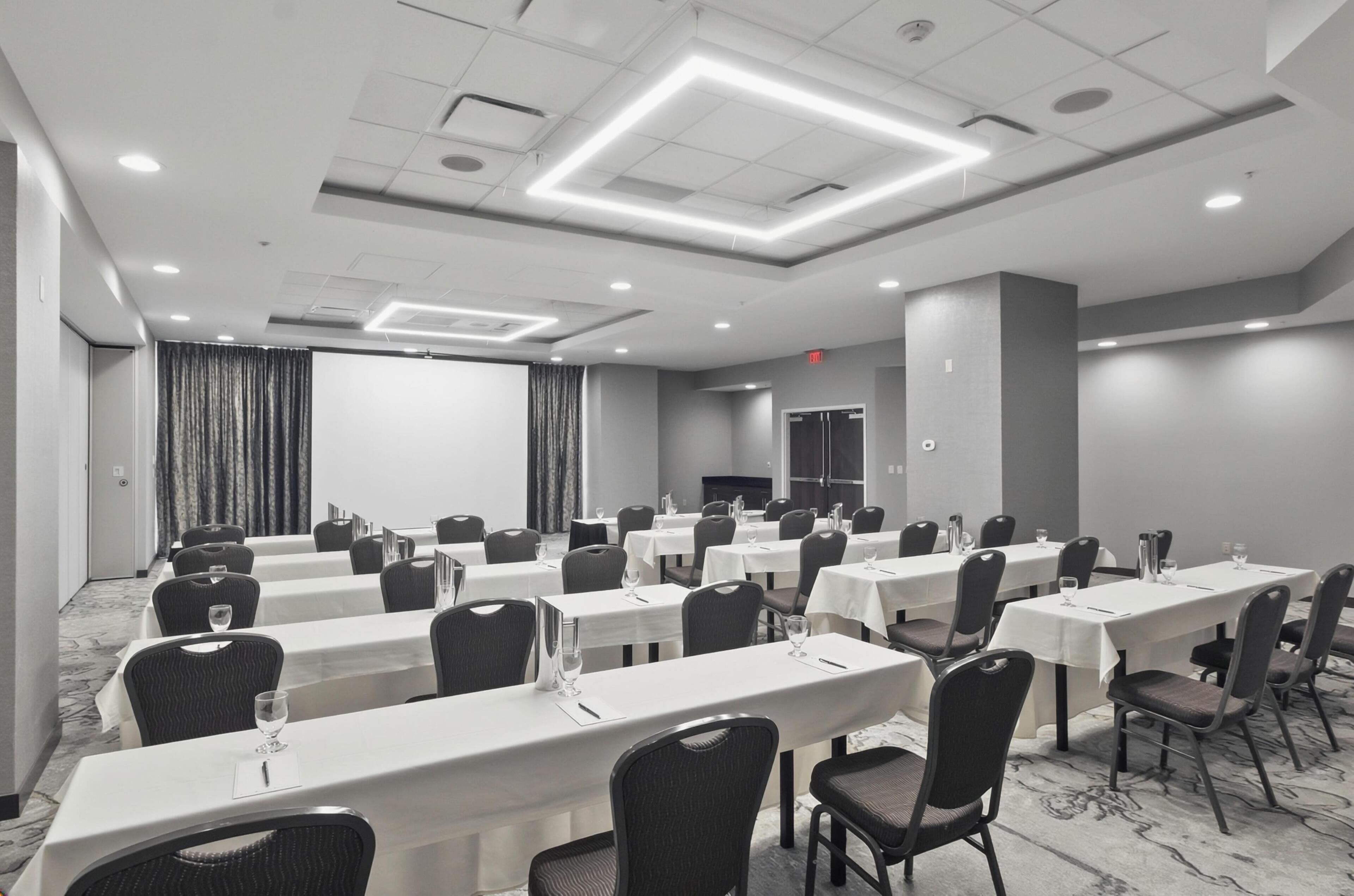 Un salón de conferencias con varias mesas, sillas y una pantalla grande.