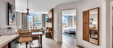 A modern hotel room with a dining area, a large bed, and a view of the city.