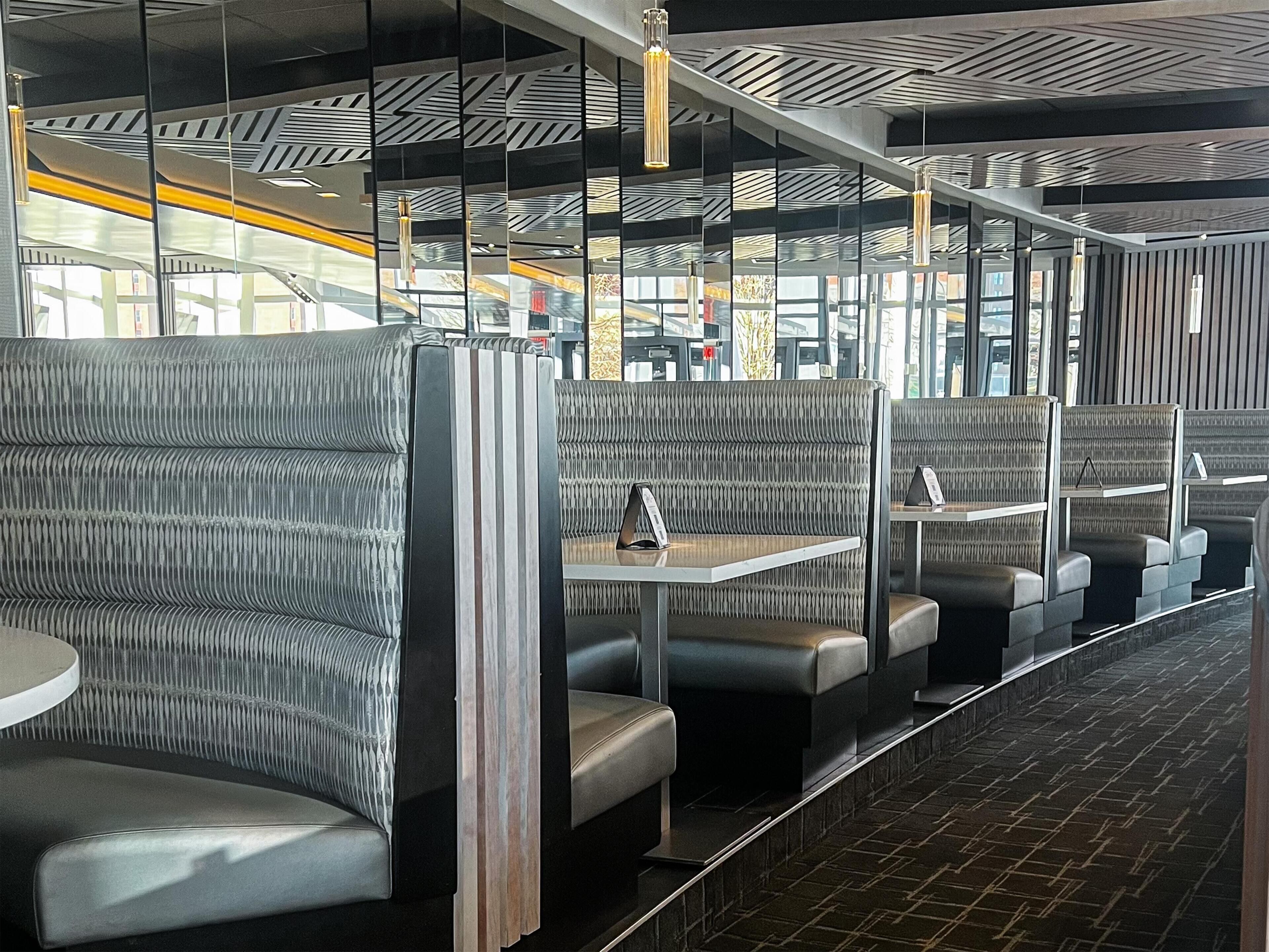 A modern restaurant with booth seating, high ceilings, and a patterned wall design.