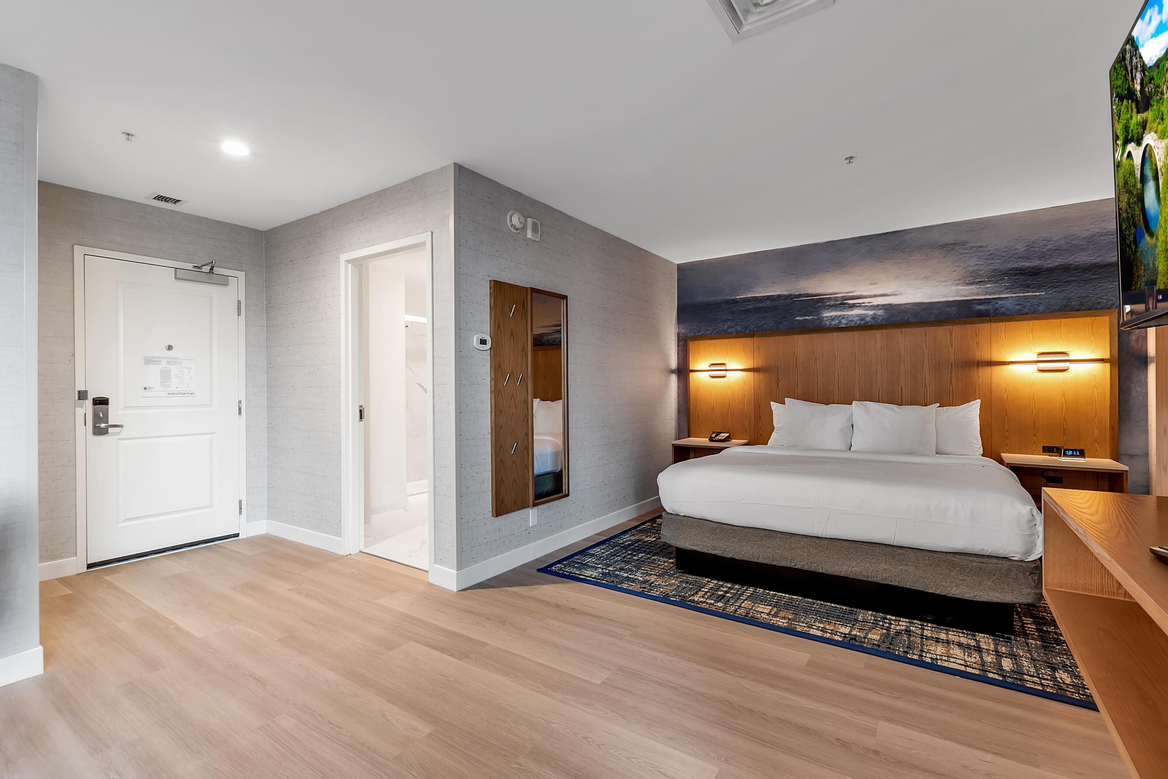 Une chambre d’hôtel moderne dotée d’un grand lit, d’une tête de lit en bois, d’un téléviseur à écran plat, d’une table de chevet et d’une porte à clé.