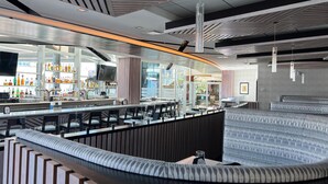 Zona de bar moderna con asientos, barra llena de botellas y un ventanal grande.